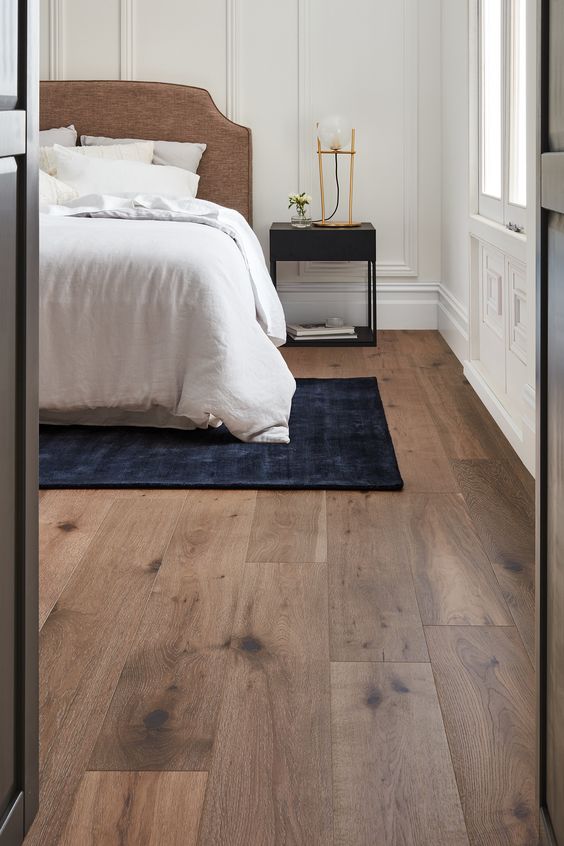 Bedroom interior featuring light brown Engineered timber flooring. A bed with a rug and nightstands are visible in the background.