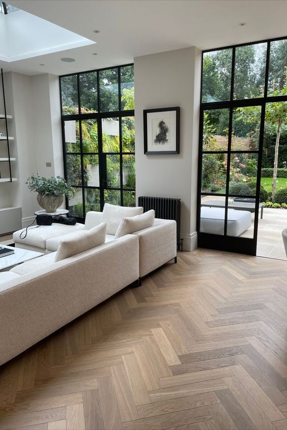 Living room interior showcasing light-colored timber flooring in herringbone pattern. A white couch and a coffee table are visible in the background.